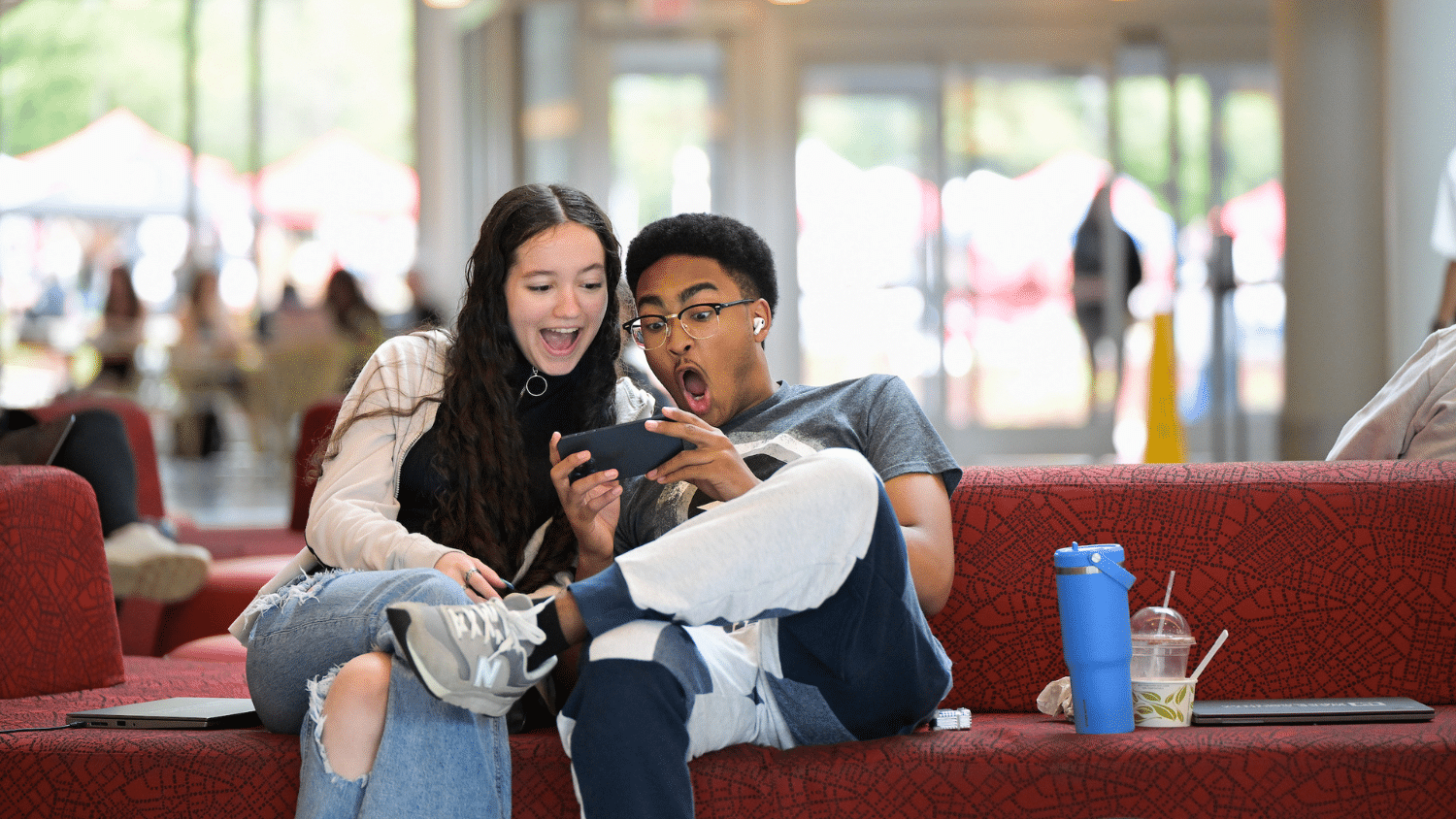 Two students sit in Talley and look at a phone together with shocked expressions.