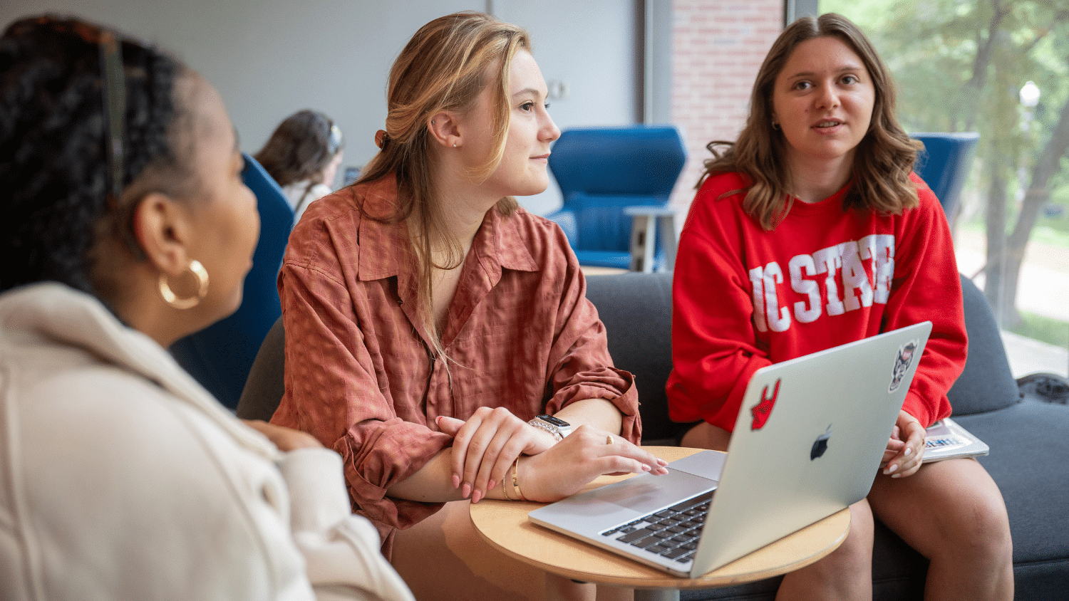 Three students chat over a laptop